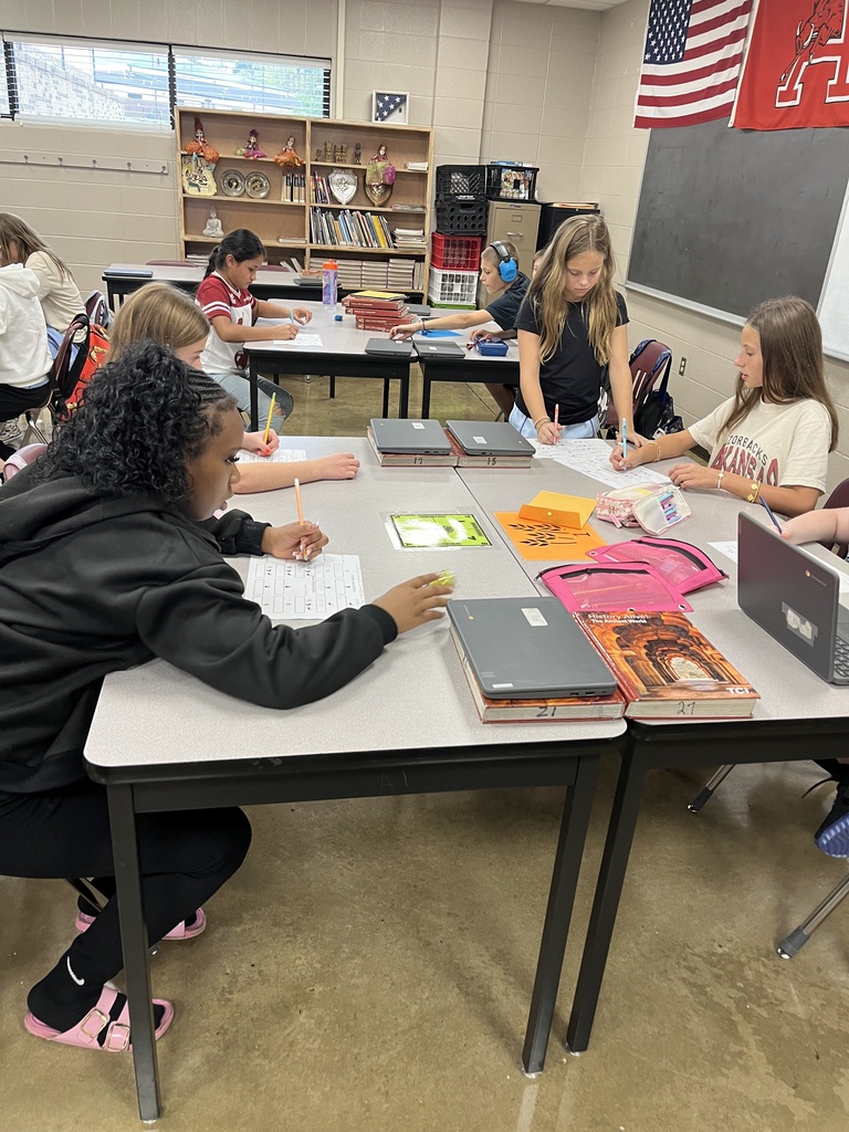 Four students gather around tables in the classroom as they work together to play a game in social studies.