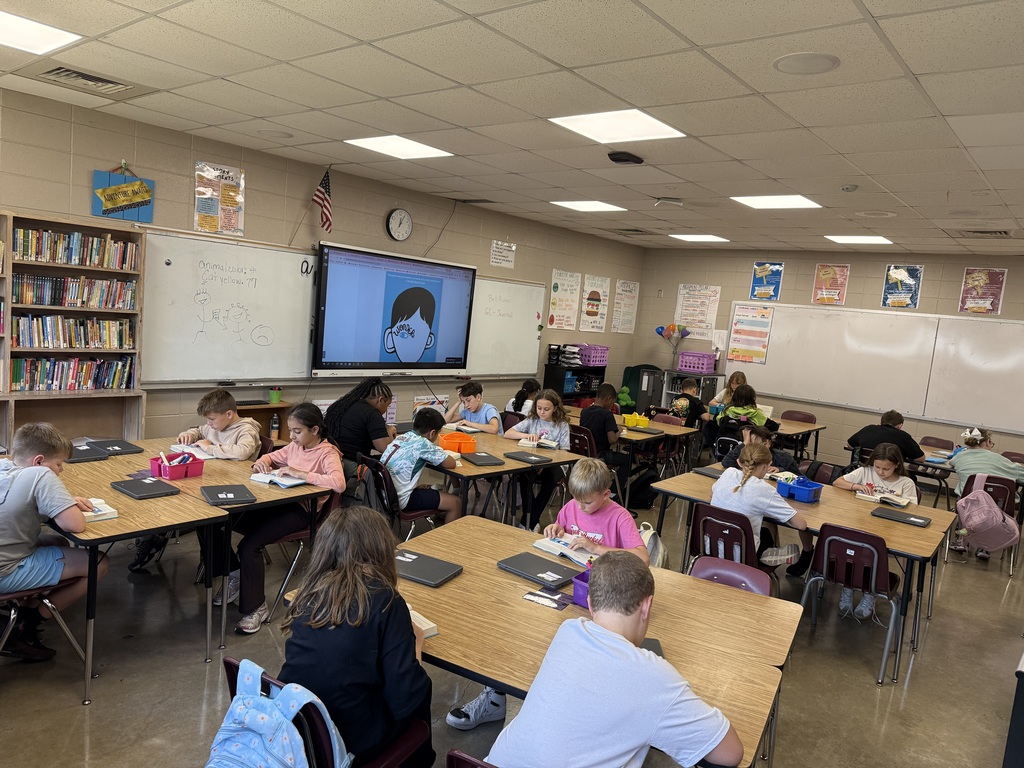 A wide view of the whole class sitting in different table groups as they are reading the book Wonder