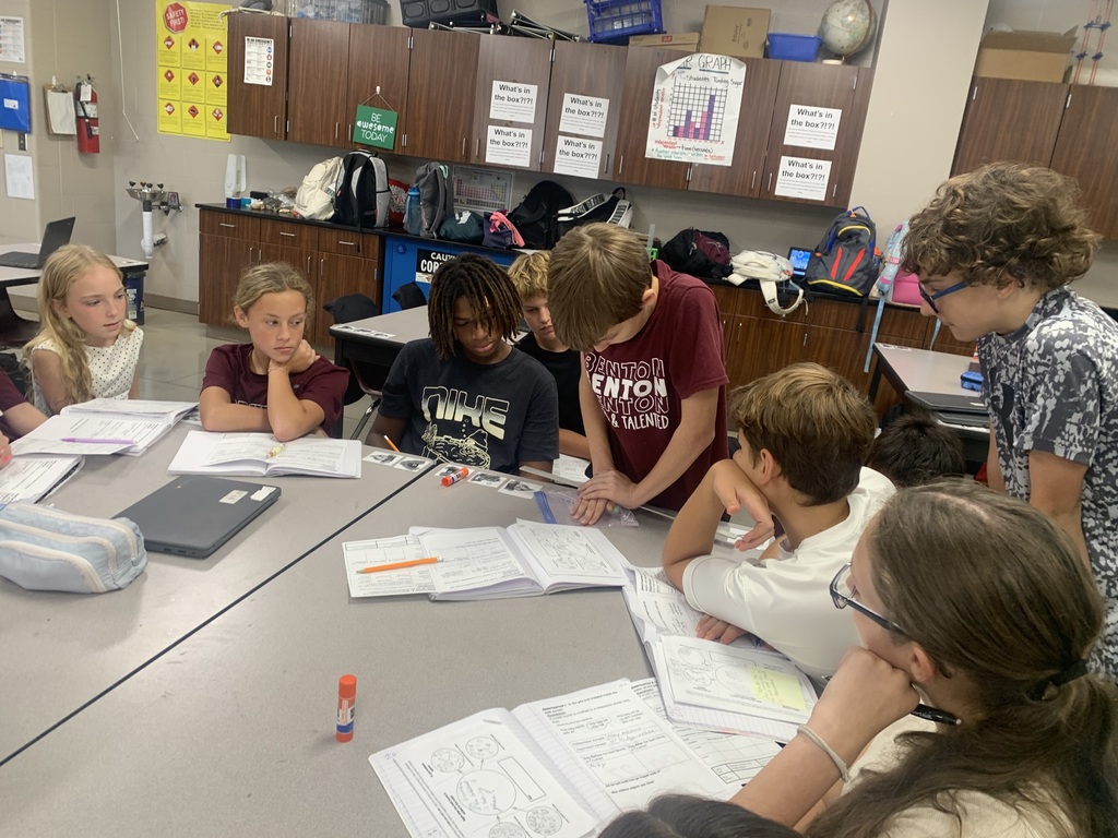 A group of students in Mr. Koch's class is gathered around a table working on their class science experiement