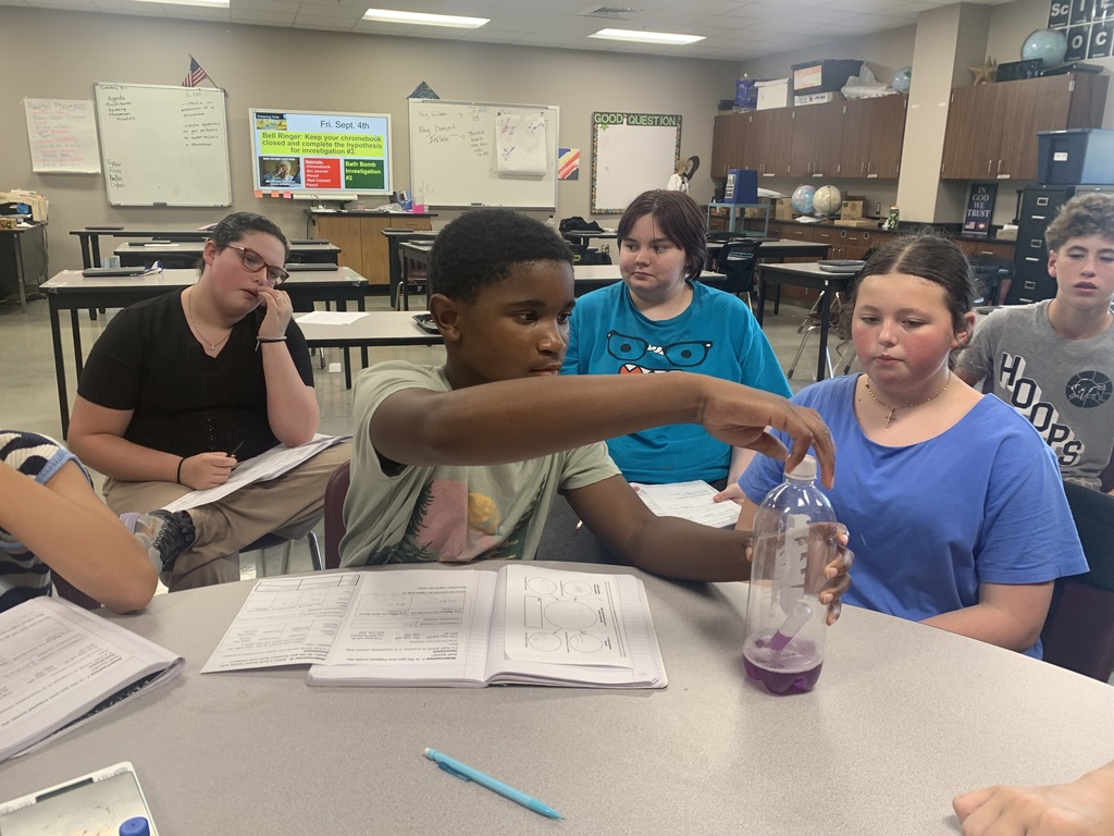 Students in Mr. Koch's class are gathered around a table as they watch a chemical reaction take place inside of a plastic bottle.