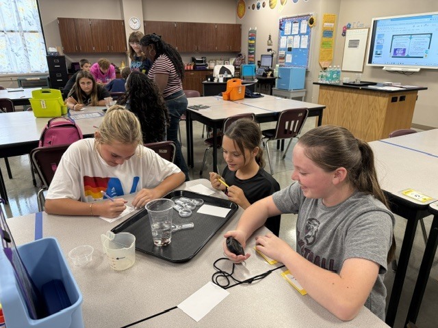Students are standing around a table in Mrs. Eddleman's class watching a science experiment.