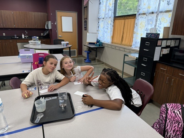 Students are standing around a table in Mrs. Eddleman's class watching a science experiment.