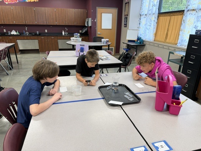 Students are standing around a table in Mrs. Eddleman's class watching a science experiment.