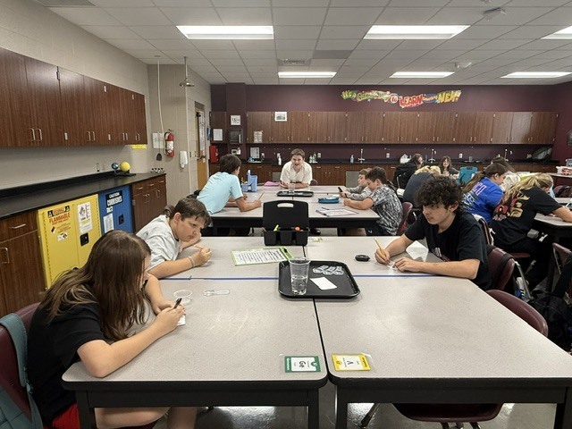 Students are standing around a table in Mrs. Eddleman's class watching a science experiment.