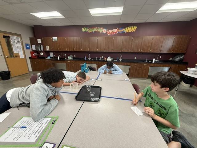 Students are standing around a table in Mrs. Eddleman's class watching a science experiment.