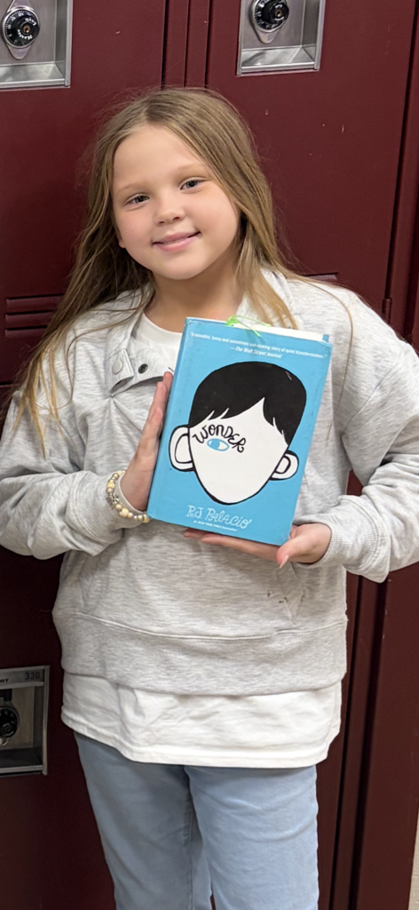 One student is smiling and displaying the cover for the book Wonder