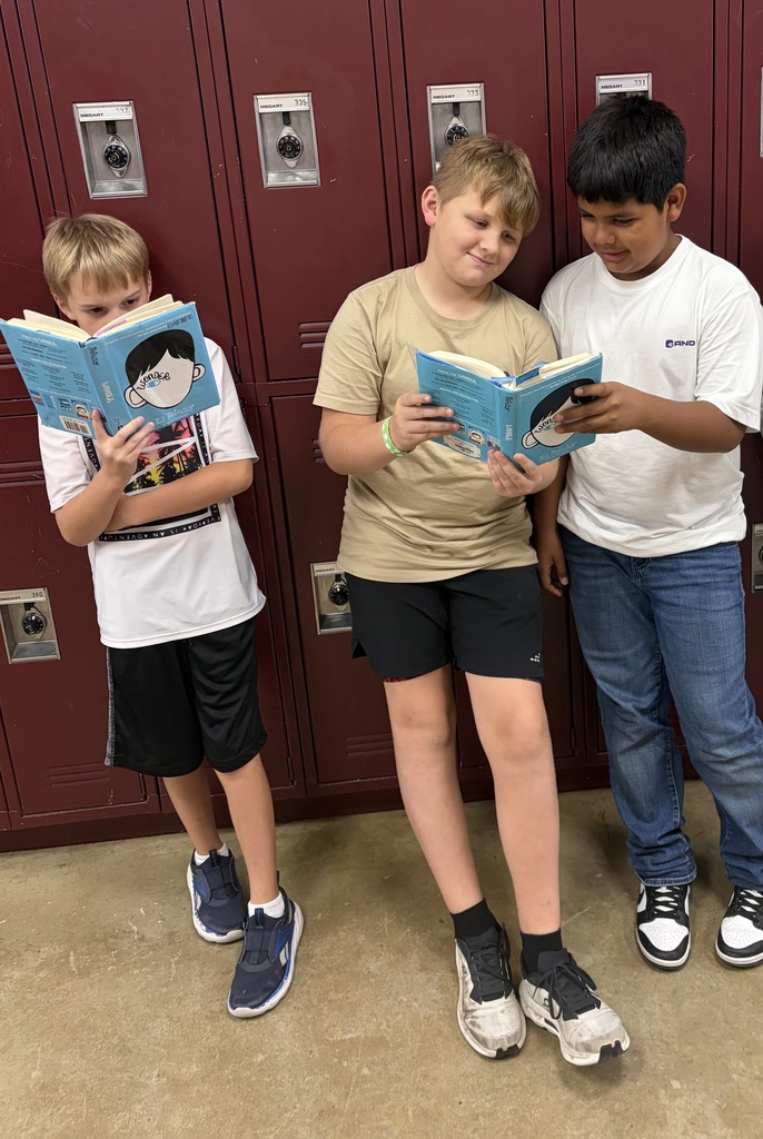 Three students are standing in the hallway reading Wonder