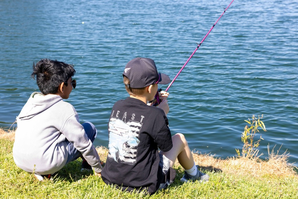 Students sitting on the bank of a pond fishing