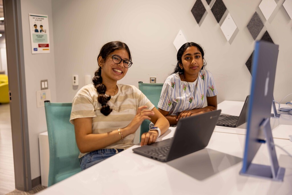 Two young female students smiling at the camera  at AI Summer Camp