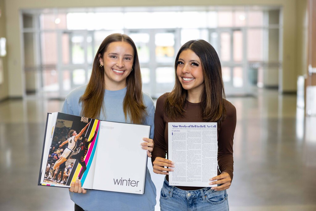 Two young ladies holding their high school yearbook and published writing report