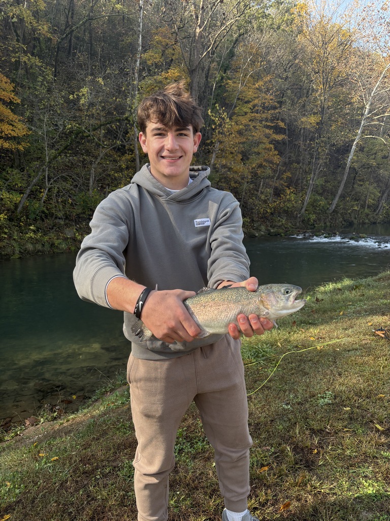 High school student holding a trout near a stream