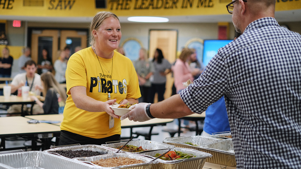Teacher being served lunch by community partners in school cafeteria.