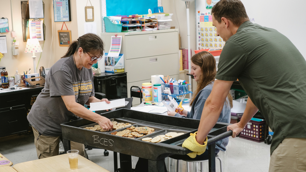 Superintendent delivering a cart of cookies to school staff in a classroom.