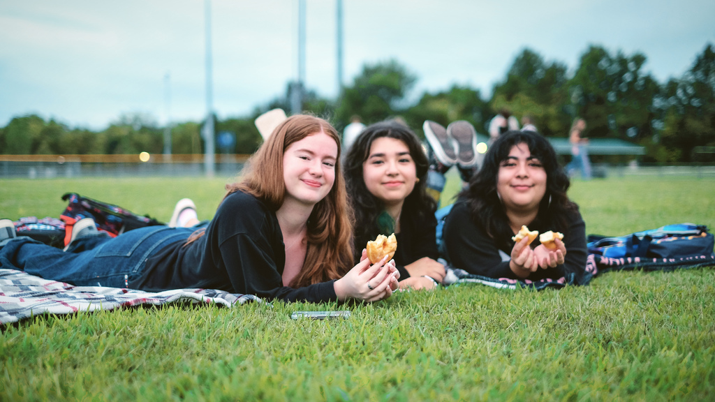 Seniors laying in grass on football field, eating donuts.