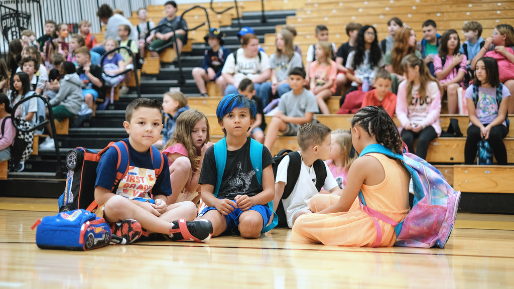 Elementary students sit attentively on gym floor.