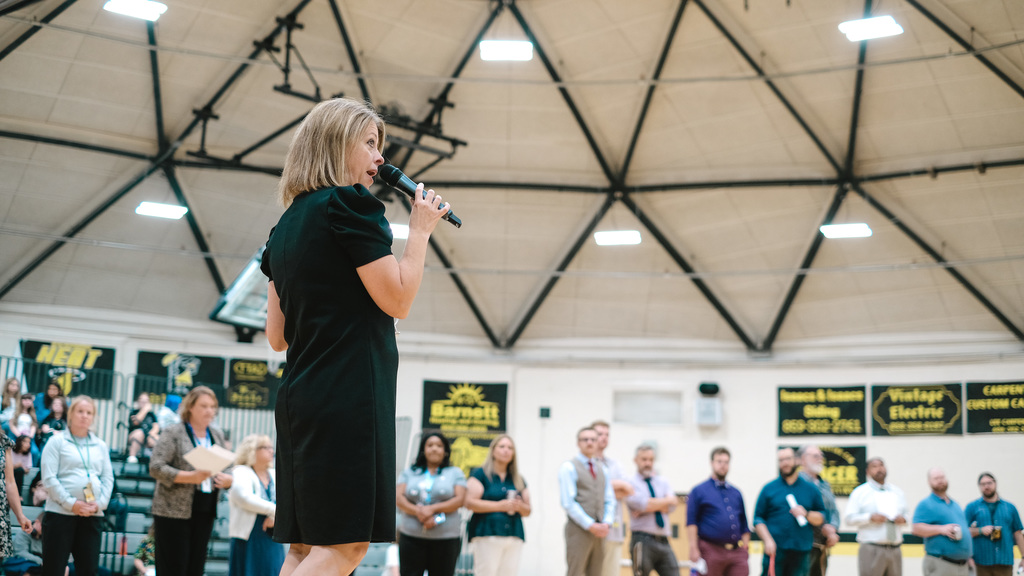 Principal holds microphone to speak to students in front of line of teachers and staff.