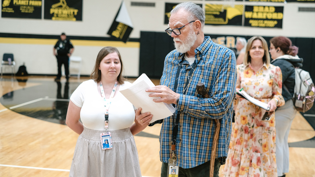 Teachers look over a stack of papers in school gym.