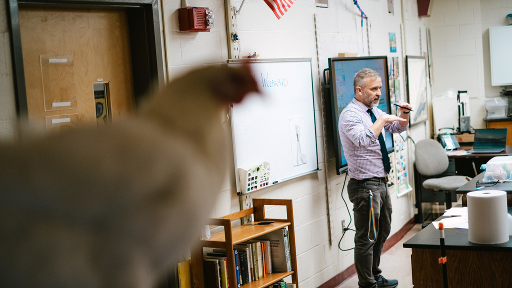 Science teacher instructs students, while a chicken looms ominously in foreground
