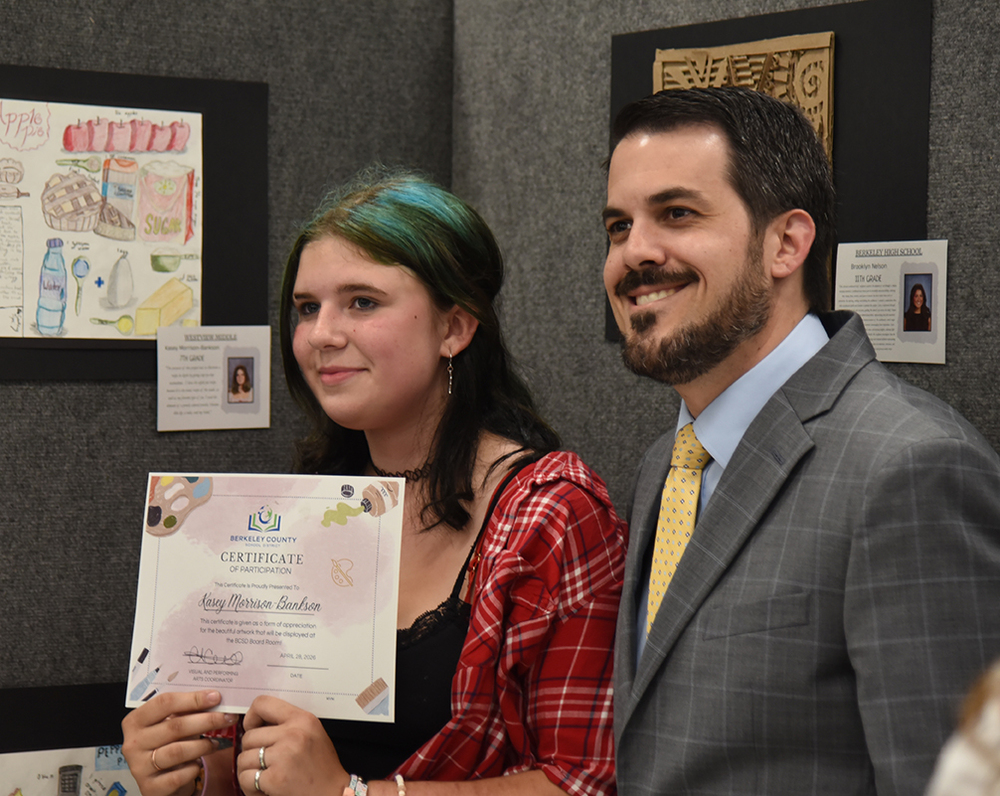 student artist with principal in front of artwork holding up certificate
