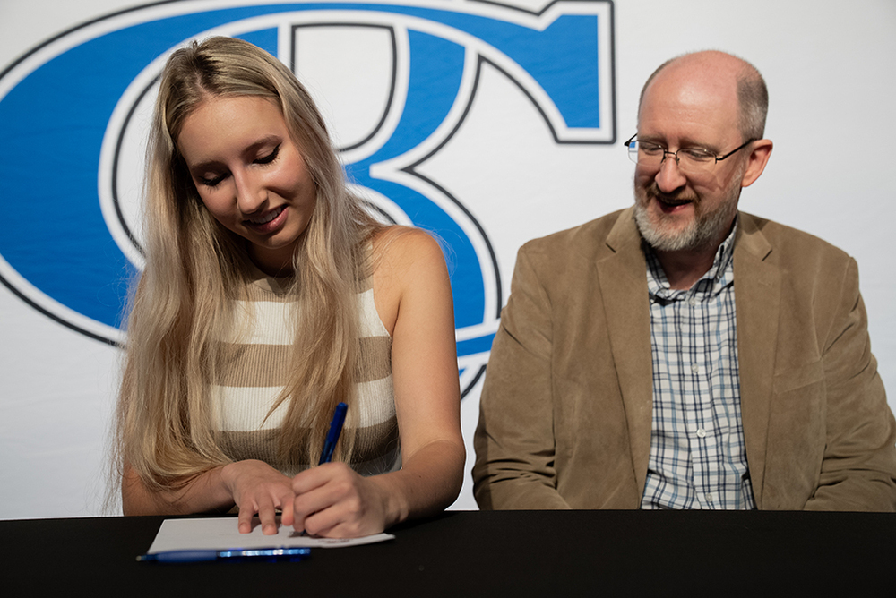 student signing letter of intent with choir director looking on
