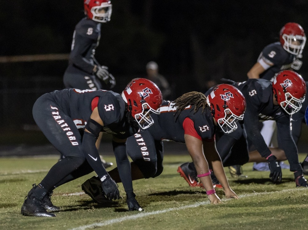 defensive linemen in black jerseys and pants with red helmets