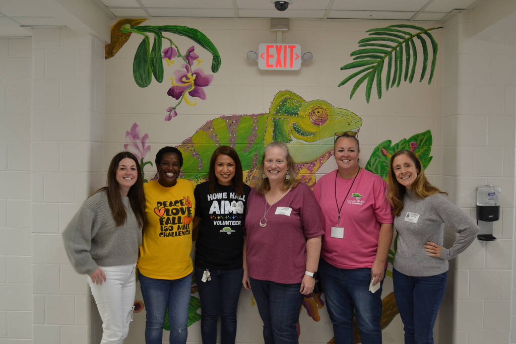 5 members of the PTA stand together smiling under the mural of a Chameleon at HHA