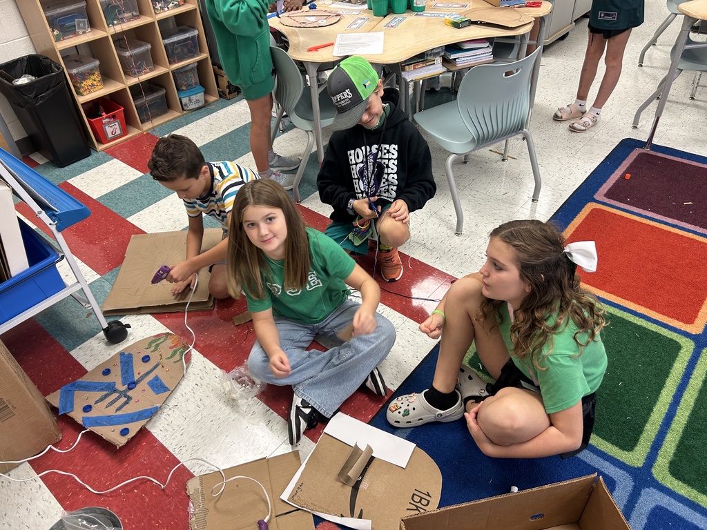 Students use recyclable materials to create shields representing cabins from a novel.
