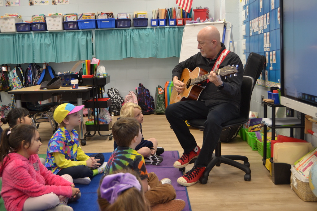 Students learning a song with an artist in residence holding a guitar