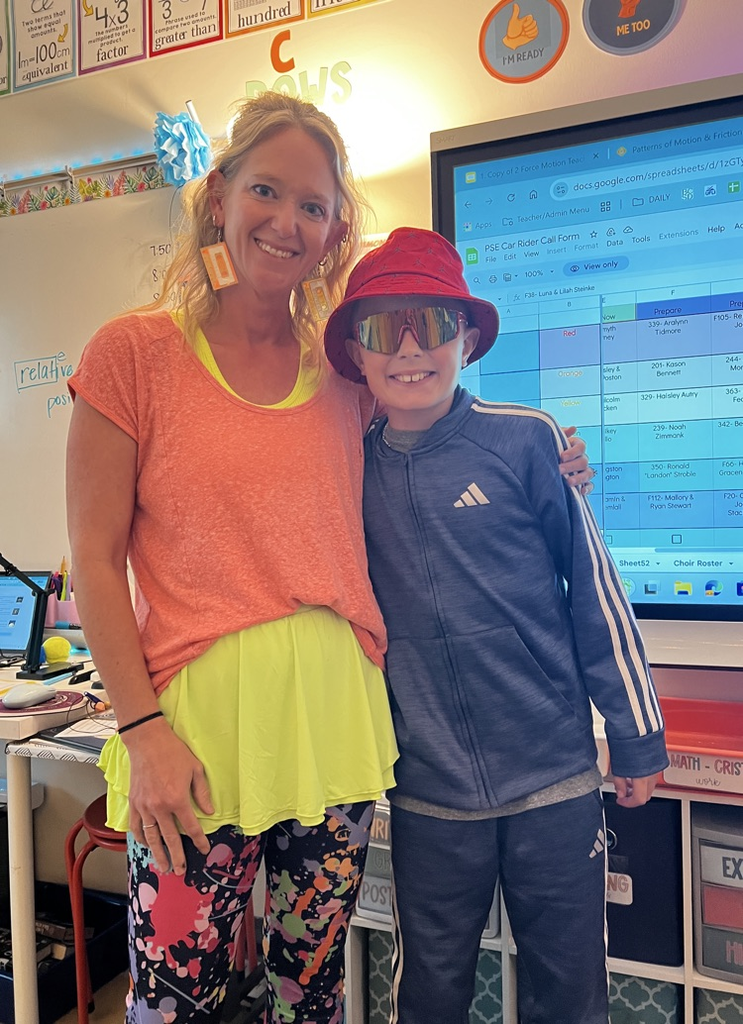 teacher in bright colors smiling with student in hat and sunglasses 
