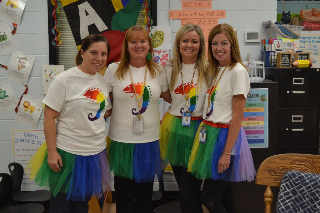 People posing for a picture wearing colorful tutus and a shirt with a chameleon on it. 