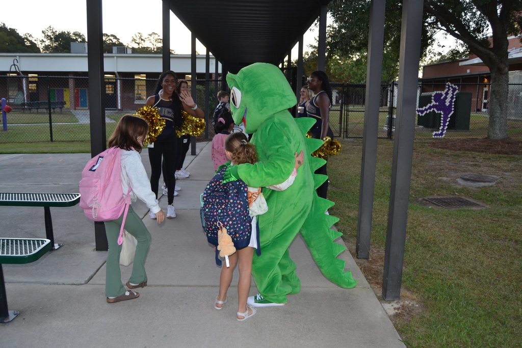 Kids hugging a mascot and people waving.