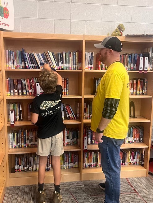 One of our volunteers helping a young boy find a book on the library shelf.
