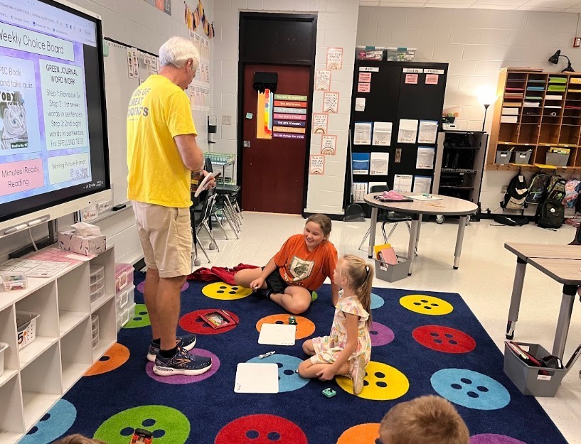 One of our volunteers working two students down on the carpet, spelling words on their whiteboards.