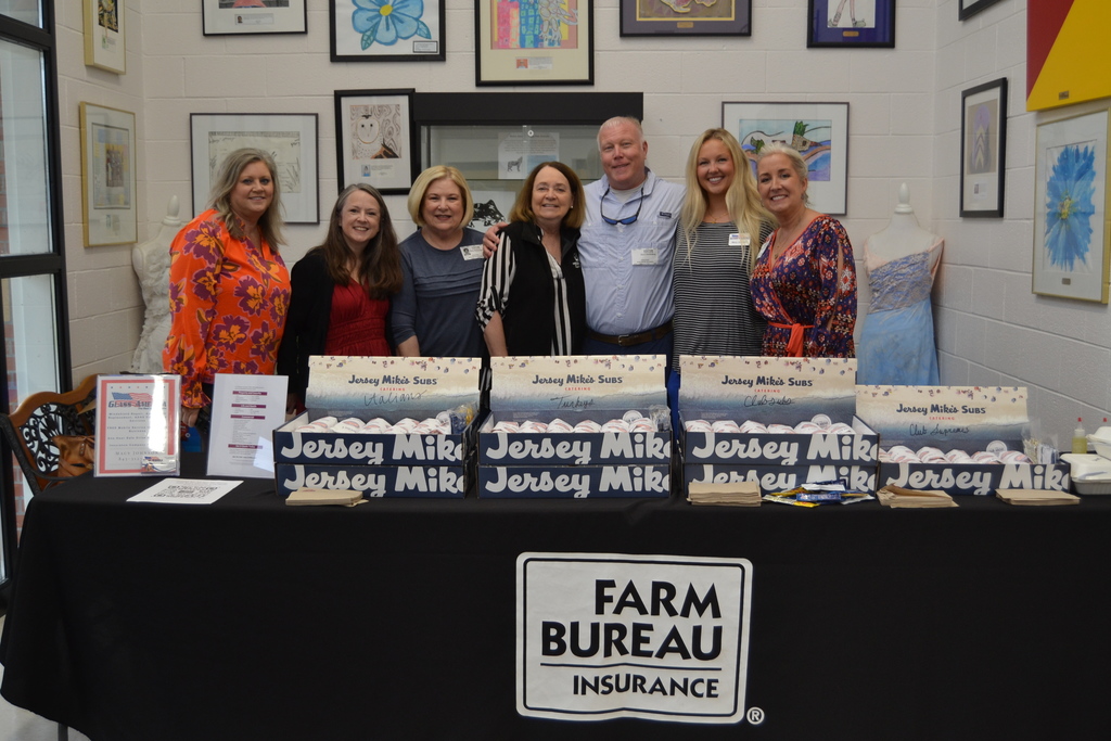People smiling for a picture in front of a Farm Bureau sign and Jersey Mike's subs