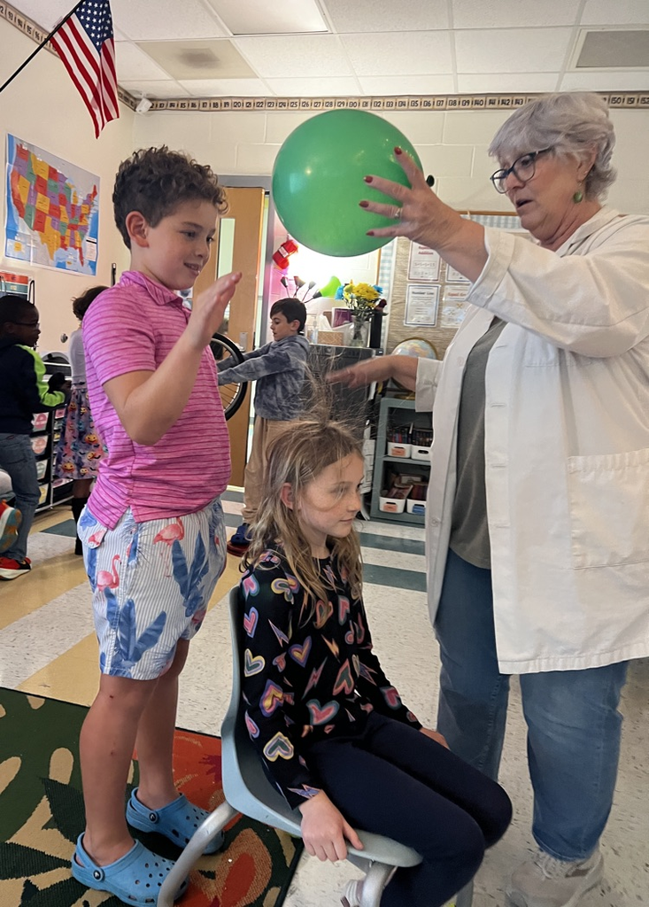 student rubbing green balloon on student’s head