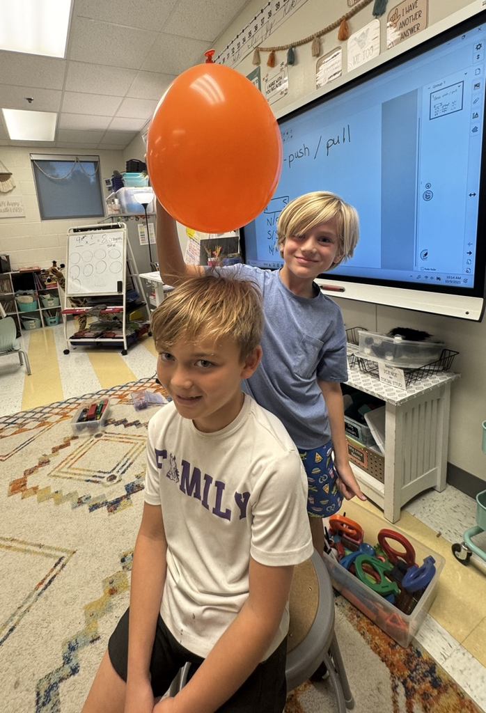 students rubbing red ballon on students head