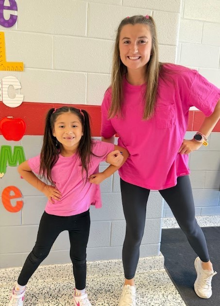 Teacher and student dressed as twins in matching bright pink shirt and pigtails