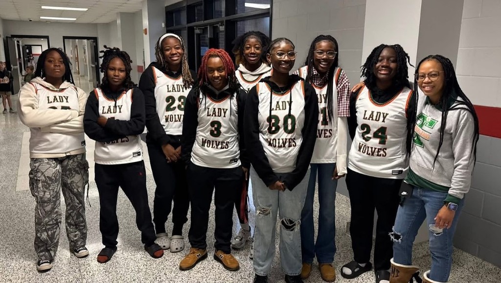 This is a group shot of the varsity girls basketball team with their coach. They each of their jerseys on, ready to show off their excitement for high fives to students.