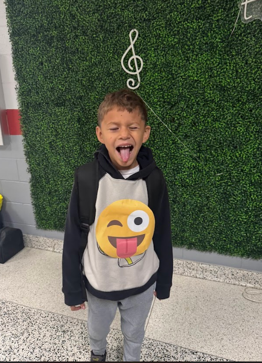 Young boy wear the winky face- tongue out emoji and makes his face the exact same as he poses for the picture.