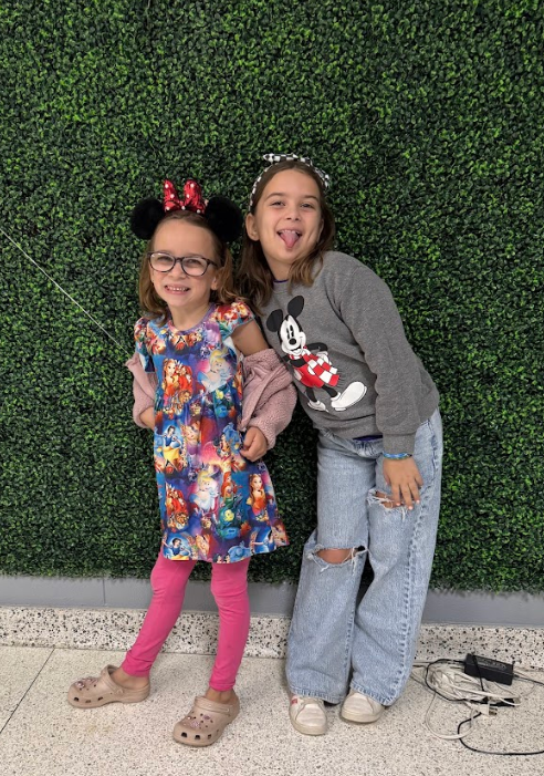 Two girls with disney ears and disney sweatshirts pose for disney day.