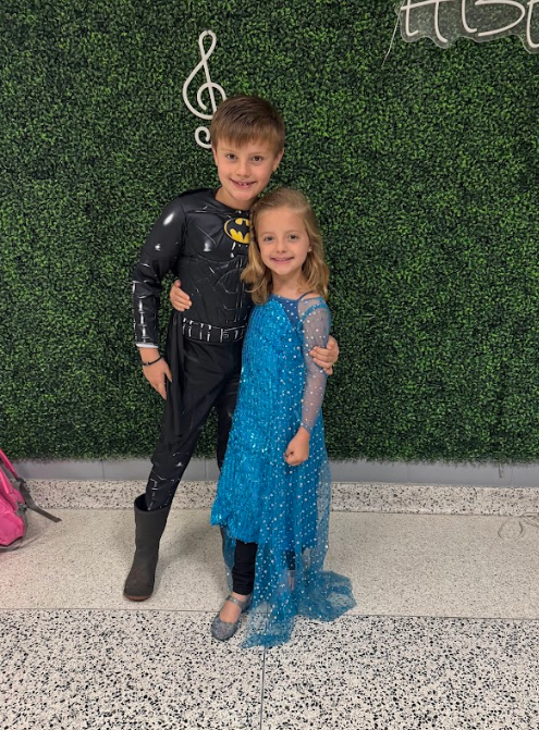Young boy and girl pose with arms around one another, the little boy is dressed as Batman and the little girl is wearing a princess dress.