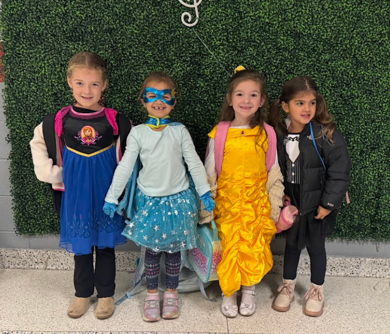 Four girls posing together with a super hero mask on one student and disney princess dresses on the others. One is dressed as Belle and the other is wearing a Anna dress from the Disney movie Frozen.