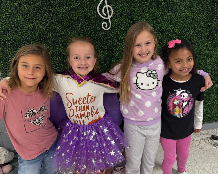 Four girls with arms wrapped around another, show off their fun disney shirts and outfits.