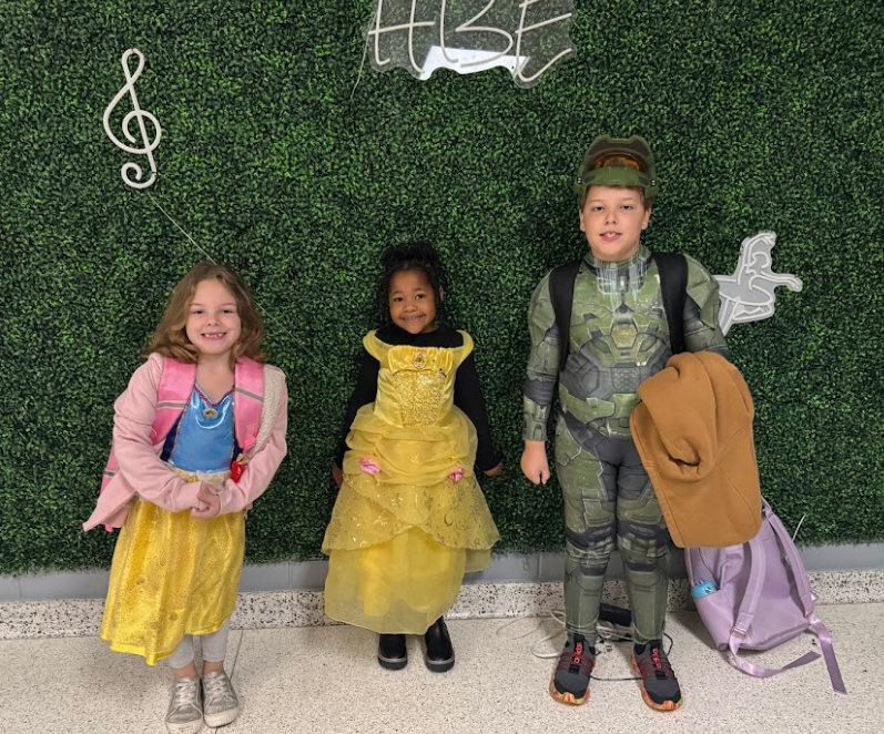 Three students, one girl is dressed as Snow White, another as Belle from Beauty and the Beast, and the young boy is wearing what looks like a military super hero outfit.