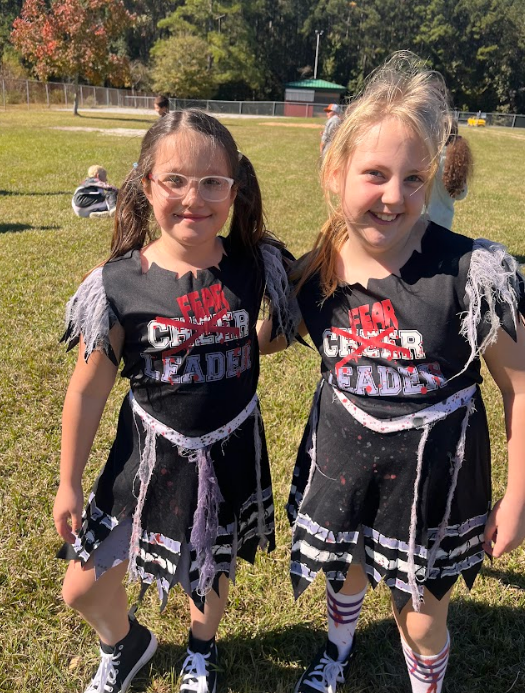 Two girls dressed as cheerleaders but their costume crosses out cheer and says "fear leader".