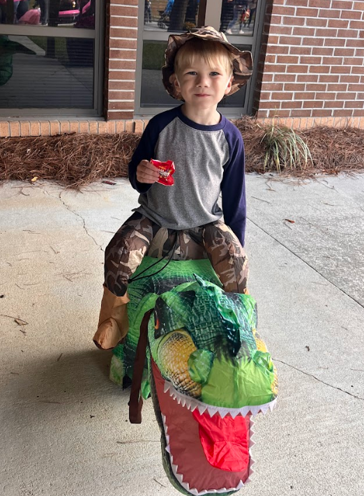 Young boy stops and smiles in his dinosaur costume.