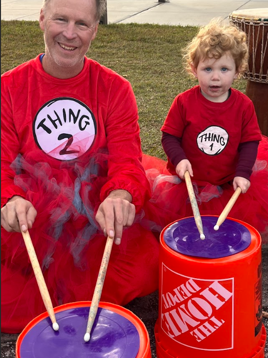 Adult & younger child dressed as thing 1 and thing 2 play the buckets at the music station.