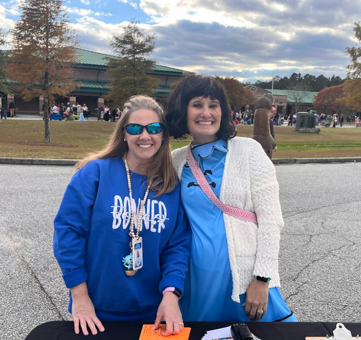 Two teachers, one with a Bonner sweatshirt and the other dressed as Lucy from Charlie Brown, smile together at the event sign-in table.