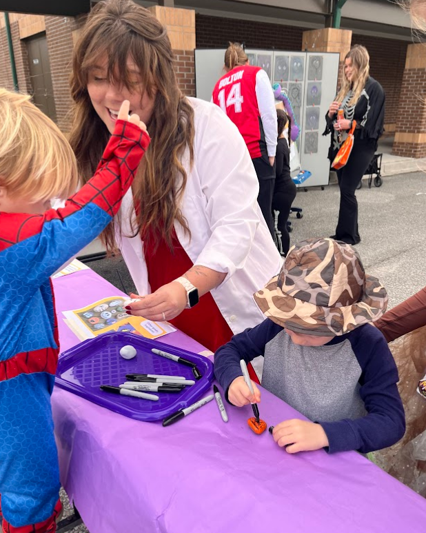 Teacher and two students are working together to add a fun spooky face to a painted rock.
