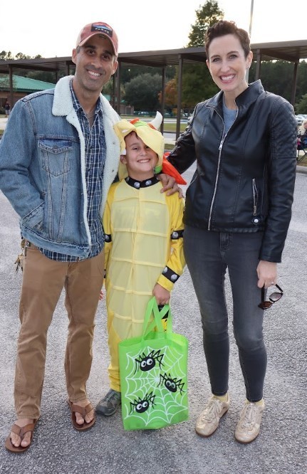 Picture of family- man, woman, and child- with child dressed as Bowser as they pose for a picture with arms around one another.